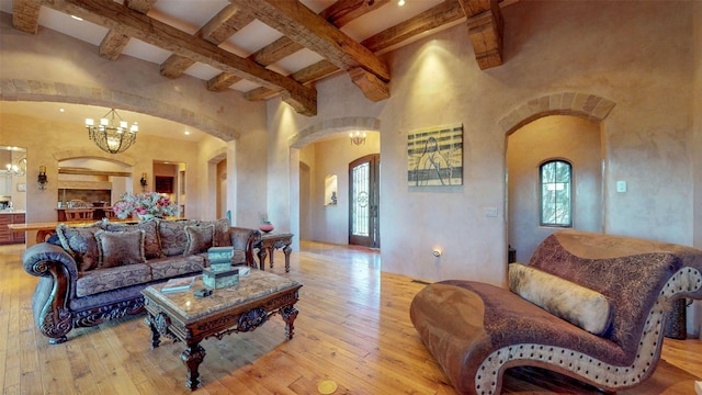 living room featuring beamed ceiling, a towering ceiling, an inviting chandelier, and light hardwood / wood-style flooring