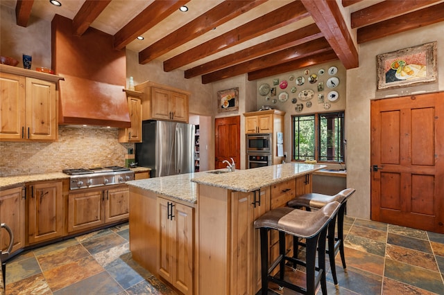 kitchen featuring a breakfast bar area, light stone counters, tasteful backsplash, a center island with sink, and stainless steel appliances