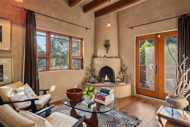 living area featuring beamed ceiling, hardwood / wood-style flooring, a fireplace, and french doors