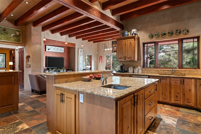 kitchen with a kitchen island with sink, sink, backsplash, and light stone counters