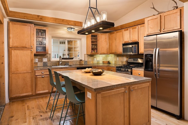 kitchen featuring lofted ceiling, sink, hanging light fixtures, stainless steel appliances, and a kitchen island