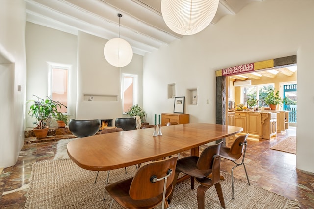 dining area with beam ceiling, a wall unit AC, and a high ceiling