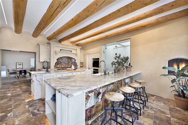 kitchen with white cabinetry, light stone countertops, sink, and beamed ceiling