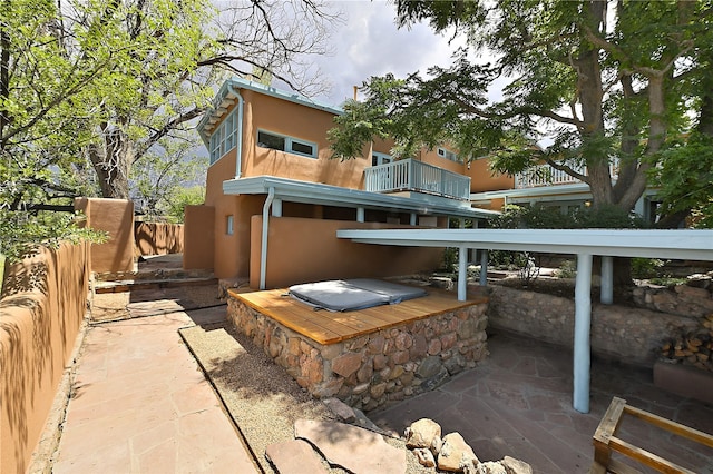 back of property with a hot tub, a patio, and a balcony