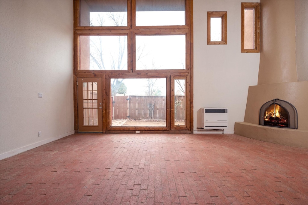 unfurnished living room with a high ceiling, a wealth of natural light, heating unit, and a fireplace