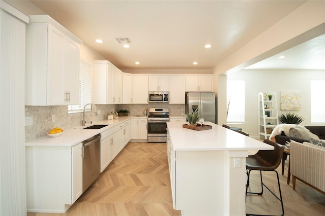 kitchen with appliances with stainless steel finishes, white cabinetry, sink, a kitchen bar, and a center island