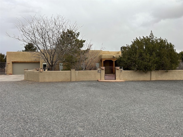 pueblo revival-style home with a fenced front yard, an attached garage, a gate, and stucco siding