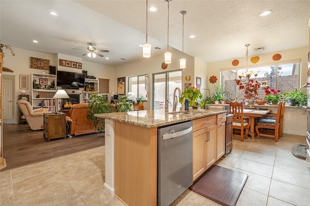 kitchen with a center island with sink, sink, stainless steel dishwasher, hanging light fixtures, and light stone countertops