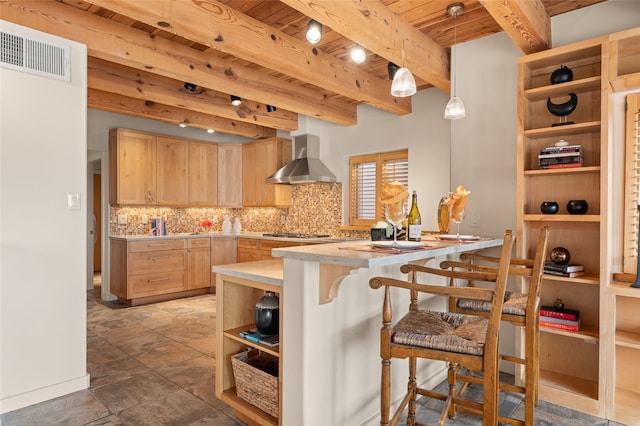 kitchen featuring decorative light fixtures, a breakfast bar, wall chimney range hood, and light brown cabinets