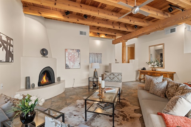 living room with a large fireplace, beamed ceiling, ceiling fan, and wood ceiling