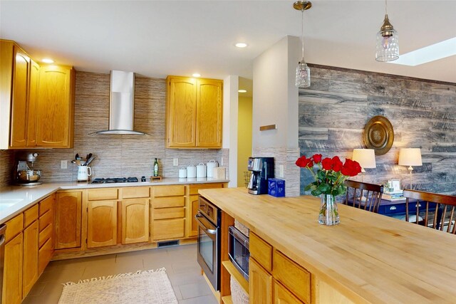 kitchen featuring butcher block counters, tasteful backsplash, appliances with stainless steel finishes, wall chimney range hood, and pendant lighting