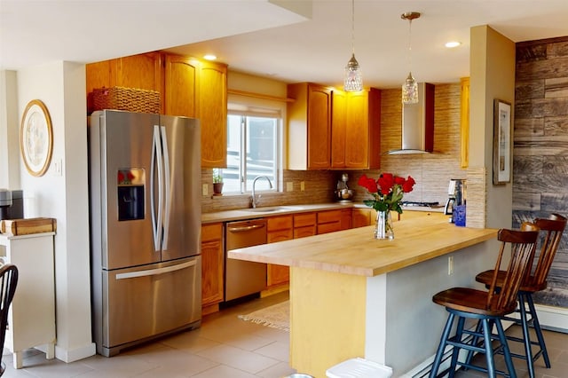 kitchen featuring stainless steel appliances, butcher block counters, backsplash, wall chimney range hood, and a kitchen breakfast bar