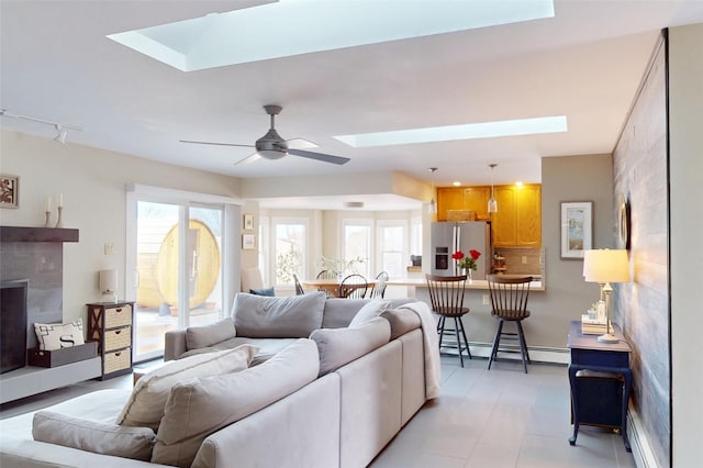 living room with a baseboard heating unit, a skylight, and ceiling fan