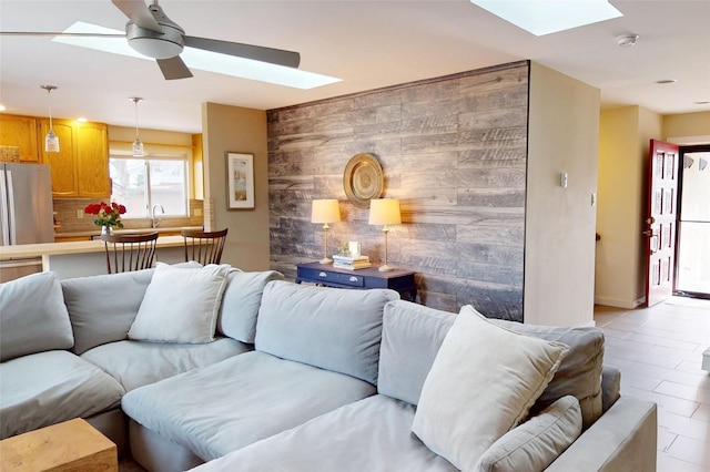 living room with sink, a skylight, wooden walls, and ceiling fan