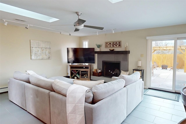 tiled living room with a baseboard heating unit, a skylight, rail lighting, and ceiling fan