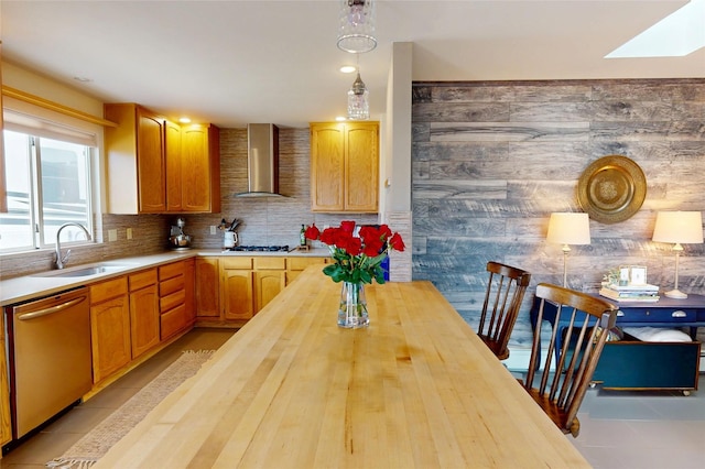 kitchen featuring sink, dishwasher, decorative light fixtures, wall chimney exhaust hood, and tasteful backsplash