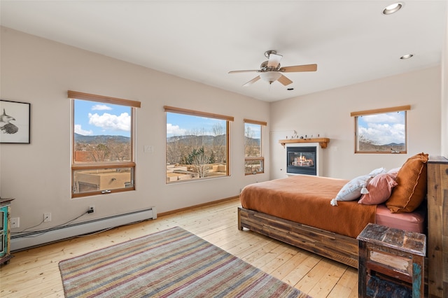 bedroom with baseboard heating, ceiling fan, light wood-type flooring, and a mountain view