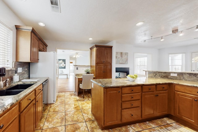 kitchen with a sink, visible vents, light stone countertops, tasteful backsplash, and brown cabinetry