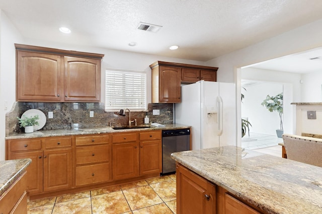 kitchen featuring white refrigerator with ice dispenser, visible vents, brown cabinetry, a sink, and dishwasher