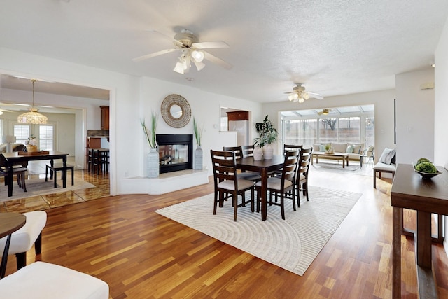 dining space featuring ceiling fan, a textured ceiling, a multi sided fireplace, and wood finished floors