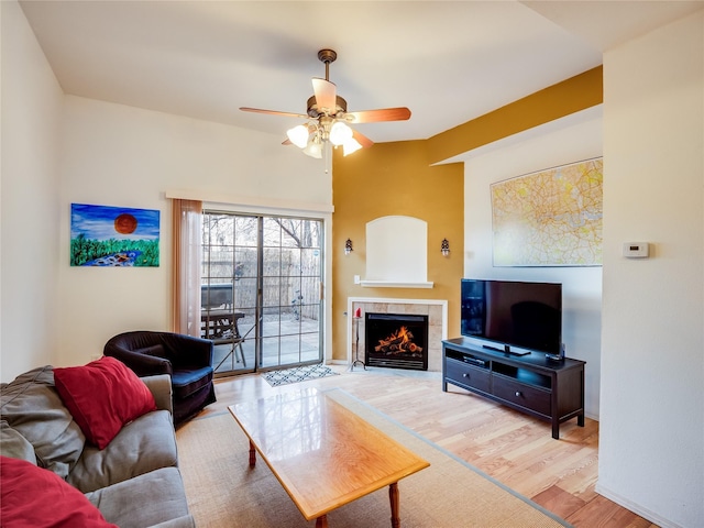 living room featuring ceiling fan, light wood-type flooring, and a tiled fireplace