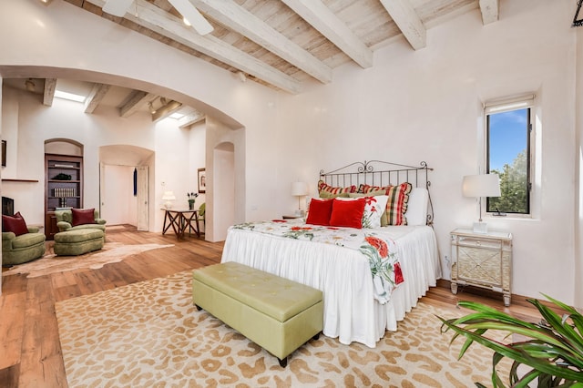 bedroom featuring arched walkways, wood ceiling, beamed ceiling, and wood finished floors