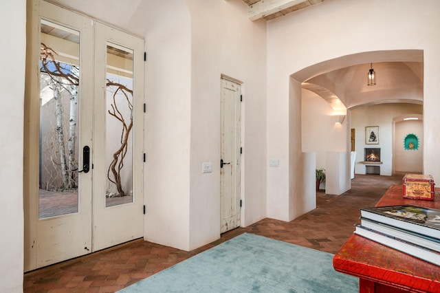 entryway featuring brick floor, arched walkways, french doors, and beamed ceiling