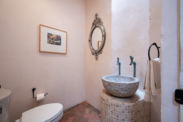 bathroom featuring brick floor, a sink, and toilet