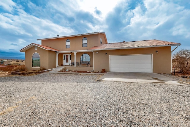 view of front facade featuring a garage, a tiled roof, gravel driveway, and stucco siding