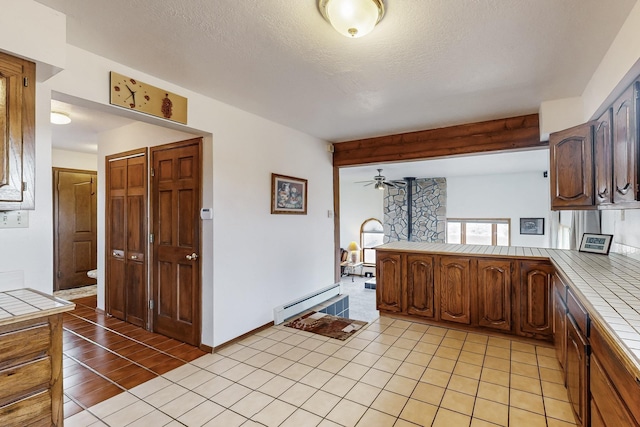 kitchen with brown cabinets, light tile patterned floors, tile counters, baseboard heating, and a peninsula