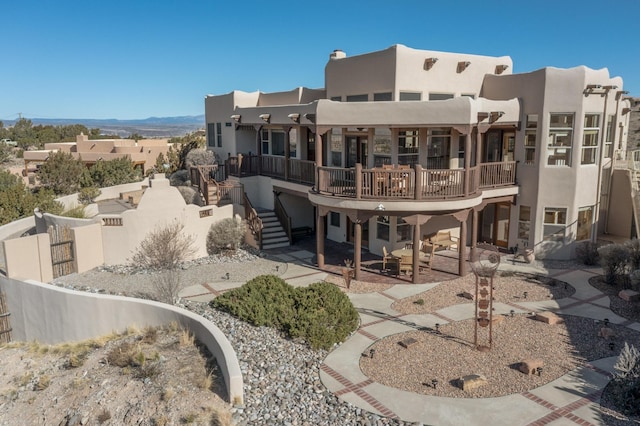 rear view of house featuring fence, stairway, and stucco siding