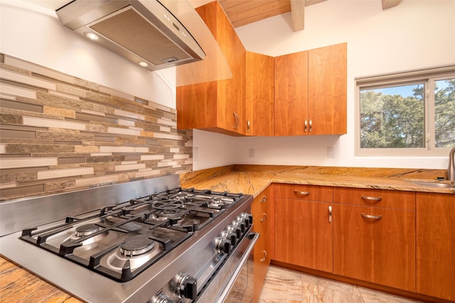 kitchen with lofted ceiling with beams, wall chimney exhaust hood, backsplash, stainless steel range with gas cooktop, and a sink