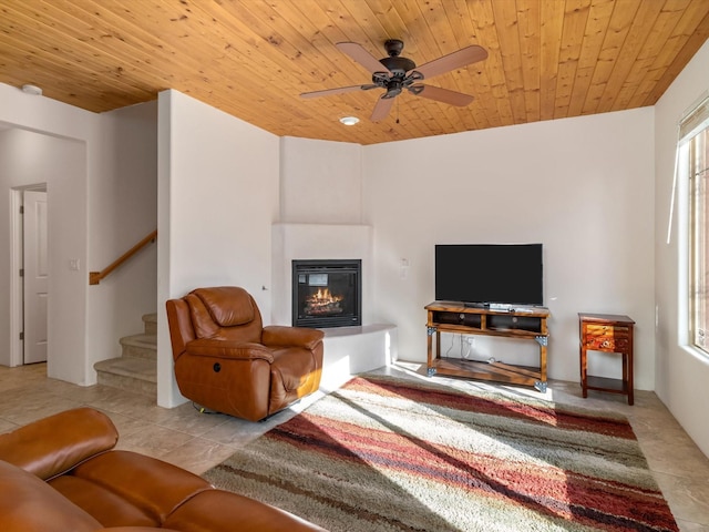 living room featuring light tile patterned floors, stairway, wooden ceiling, and a glass covered fireplace