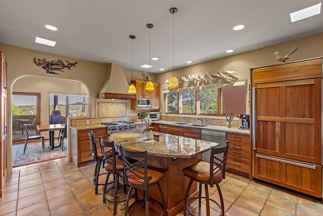 972 Indian Ridge Rd, Santa Fe, NM 87501 - kitchen featuring custom exhaust hood, appliances with stainless steel finishes, a sink, a kitchen island, and light stone countertops