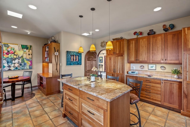 972 Indian Ridge Rd, Santa Fe, NM 87501 - kitchen with brown cabinetry, pendant lighting, a kitchen island, and light stone counters