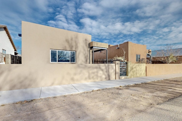 view of side of home featuring a fenced front yard, a gate, and stucco siding