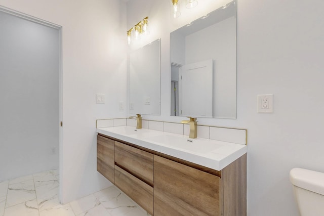 full bath featuring double vanity, marble finish floor, toilet, and a sink