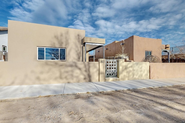 view of side of home featuring a fenced front yard, a gate, and stucco siding