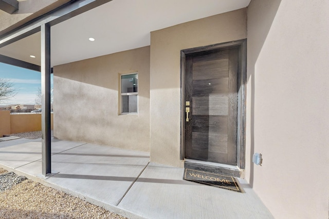 entrance to property featuring a patio area, fence, and stucco siding