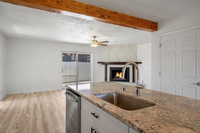 kitchen with light stone counters, open floor plan, stainless steel dishwasher, white cabinetry, and a sink