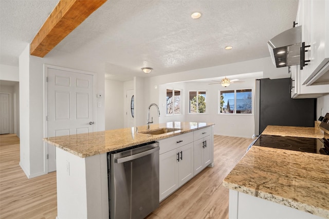 kitchen with stainless steel appliances, a sink, white cabinets, light stone countertops, and a center island with sink