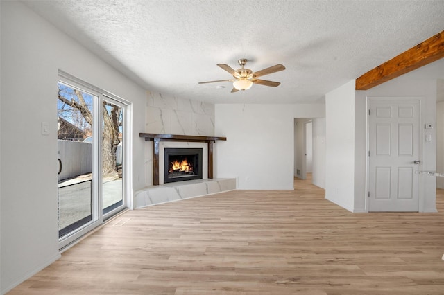 unfurnished living room featuring a ceiling fan, a fireplace, a textured ceiling, and light wood finished floors