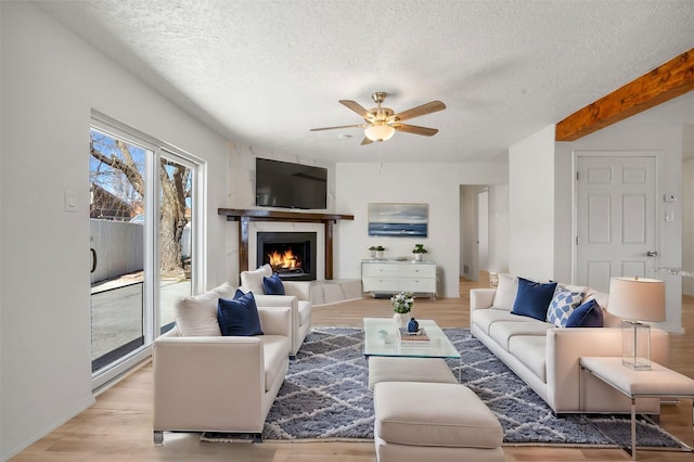 living room featuring a warm lit fireplace, ceiling fan, a textured ceiling, and light wood-style floors