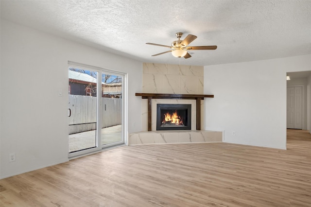 unfurnished living room with a textured ceiling, light wood-type flooring, a fireplace, and a ceiling fan