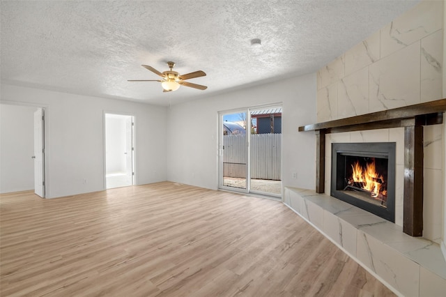 unfurnished living room with light wood-type flooring, ceiling fan, a textured ceiling, and a tile fireplace