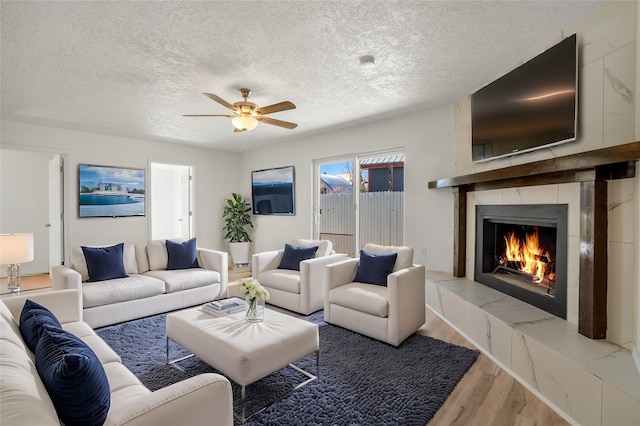 living area with a ceiling fan, a fireplace, a textured ceiling, and wood finished floors