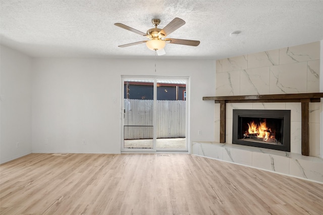 unfurnished living room featuring a textured ceiling, light wood finished floors, a premium fireplace, and a ceiling fan