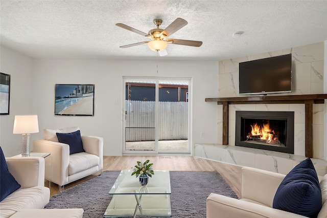 living room featuring a high end fireplace, ceiling fan, a textured ceiling, and wood finished floors