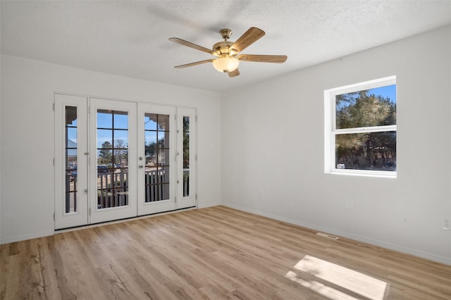 spare room with light wood-style floors, a wealth of natural light, a textured ceiling, and baseboards