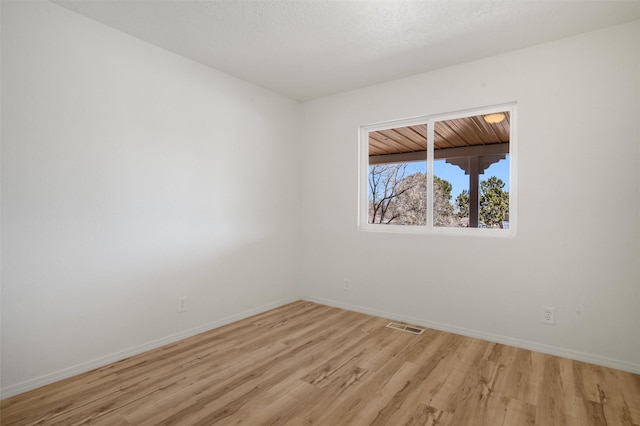 empty room featuring visible vents, light wood-style flooring, baseboards, and a textured ceiling